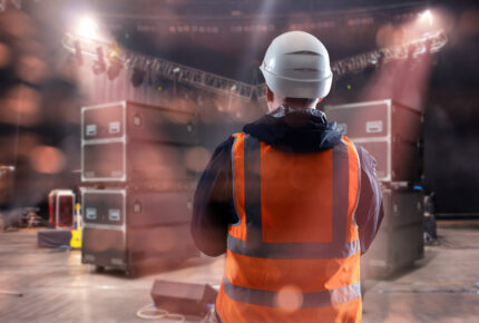 Stage technician in safety vest and helmet supervises equipment setup for an event
